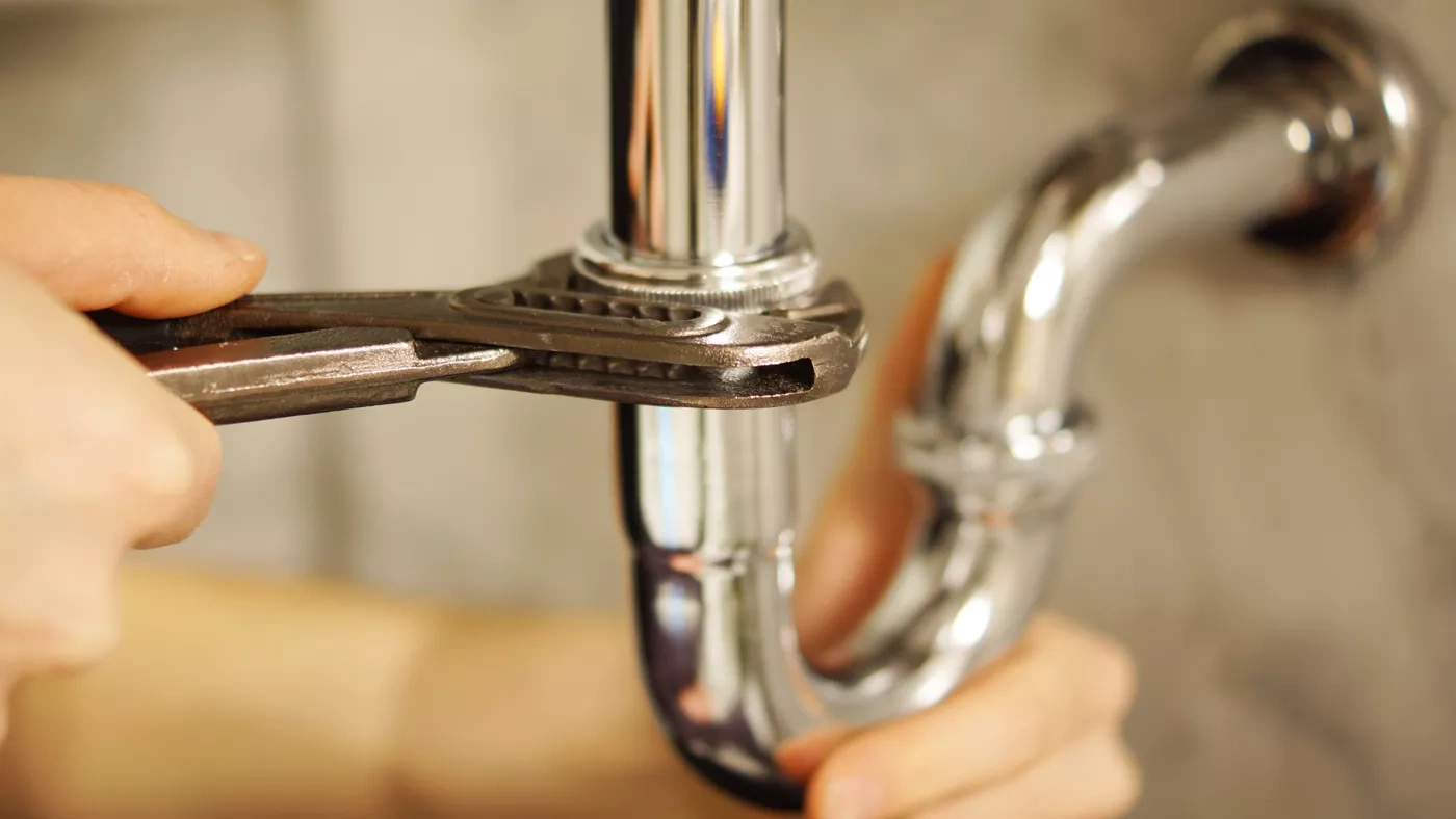 Hands holding a pipe wrench around a drain pipe